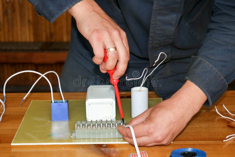Un electricista del hombre que trabaja trabajos, recoge el circuito eléctrico de una lámpara de calle blanca grande con los alamb fotos de archivo Un electricista del hombre que trabaja trabajos, recoge el circuito eléctrico de una lámpara de calle blanca grande con los alamb fotos de archivo