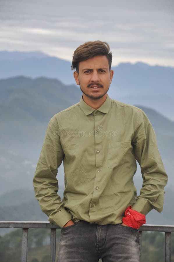 Un encantador joven indio mirando la cámara con las manos en el bolsillo mientras estaba parado en el fondo de las montañas fotos de archivo