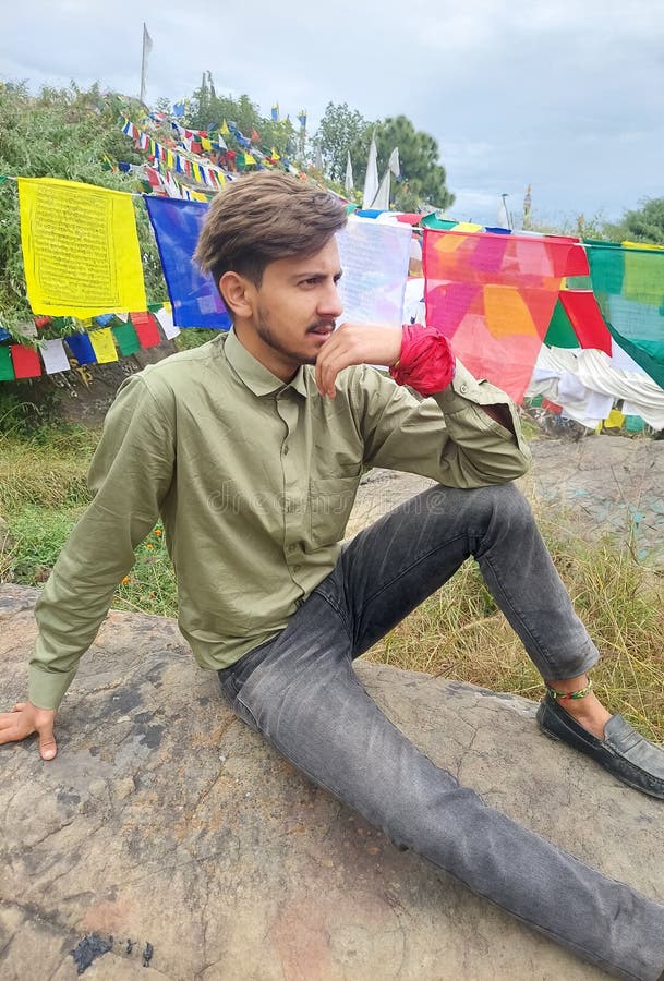 Un encantador joven mirando de costado mientras estaba sentado en una roca con el fondo de banderas budistas de oración en rewalsa foto de archivo libre de regalías