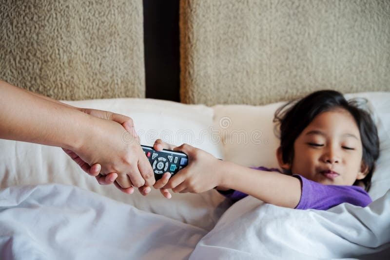 Un enfant asiatique au lit veut reprendre le contrôle de la télévision de ses mains Concept de dépendance ou de contrôle parental image stock Un enfant asiatique au lit veut reprendre le contrôle de la télévision de ses mains Concept de dépendance ou de contrôle parental image stock