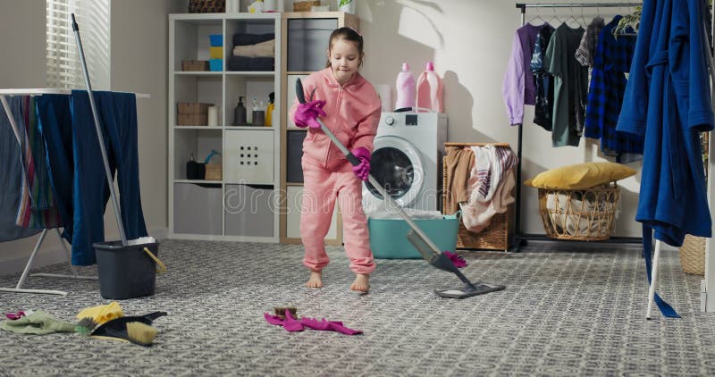 Un enfant souriant et heureux passe du temps dans la buanderie à faire les tâches ménagères. une fille en sweat rose tient une ser banque de vidéos