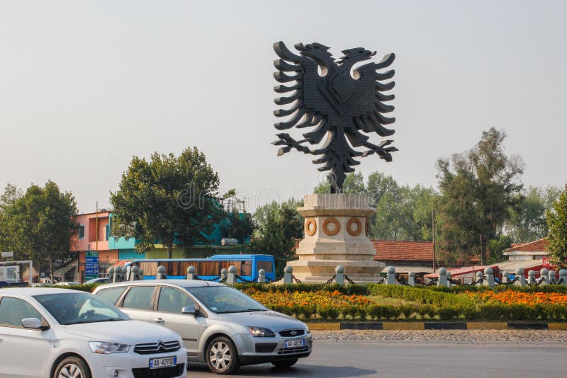 Un'enorme statua raffigurante il simbolo nazionale con la bandiera - un'aquila nera per la strada tra le macchine sulla strada immagine stock libera da diritti Un'enorme statua raffigurante il simbolo nazionale con la bandiera - un'aquila nera per la strada tra le macchine sulla strada immagine stock libera da diritti