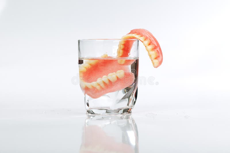 Un ensemble de dentiers dans un verre de l'eau photo stock Un ensemble de dentiers dans un verre de l'eau photo stock