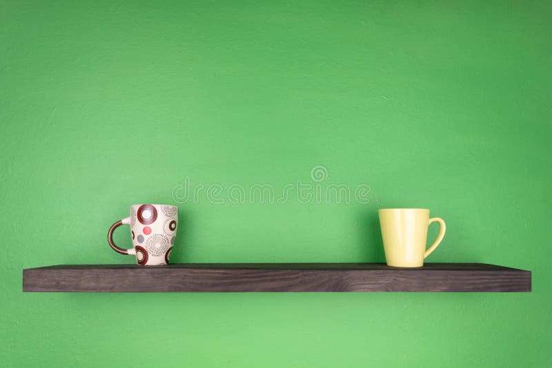 Un estante del color oscuro con texturizar la madera está instalado en una pared verde; en el estante hay dos tazas diferentement fotografía de archivo libre de regalías Un estante del color oscuro con texturizar la madera está instalado en una pared verde; en el estante hay dos tazas diferentement fotografía de archivo libre de regalías
