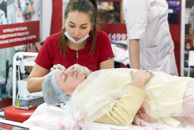 Un estetista del chirurgo mostra su una donna dell'età avanzata i metodi di ringiovanimento e di sollevamento della pelle immagine stock Un estetista del chirurgo mostra su una donna dell'età avanzata i metodi di ringiovanimento e di sollevamento della pelle immagine stock
