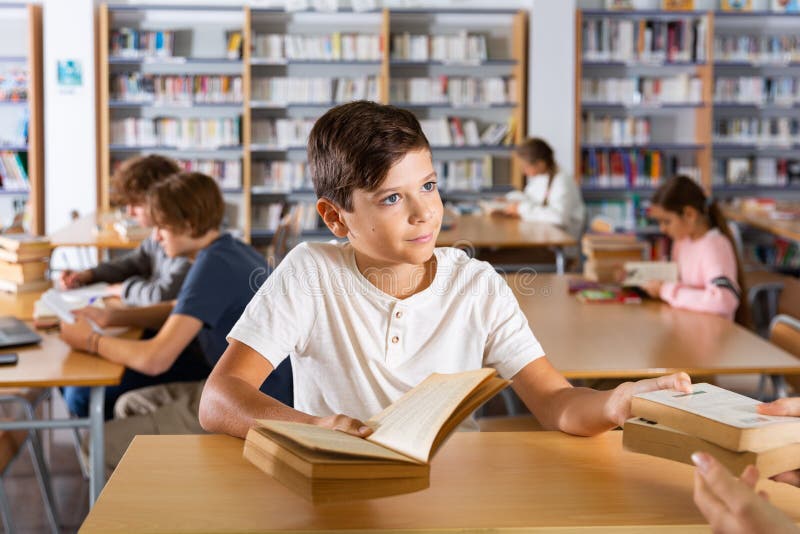 Ten-year-old schoolboy who came to the school library passes books to the librarian. Ten-year-old schoolboy who came to the school library passes books to the librarian