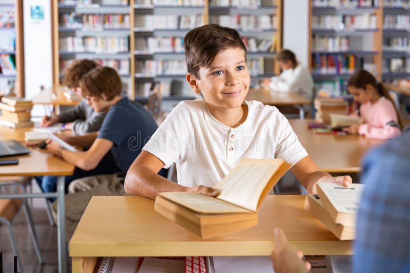 Ten-year-old schoolboy who came to the school library passes books to the librarian. Ten-year-old schoolboy who came to the school library passes books to the librarian