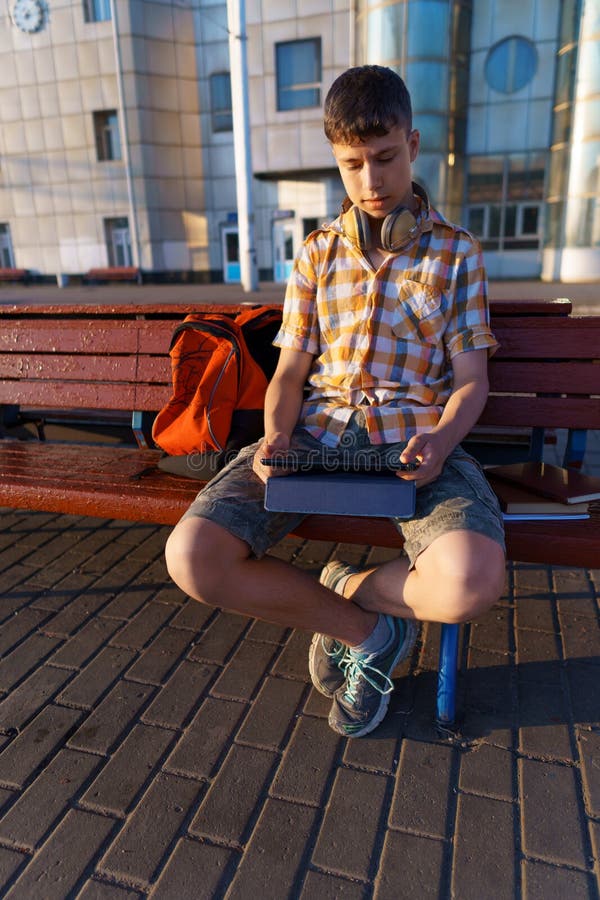 Un estudiante de escuela en la estación de tren que un niño está esperando por un tren en la plataforma usa una tableta y hace los imagen de archivo