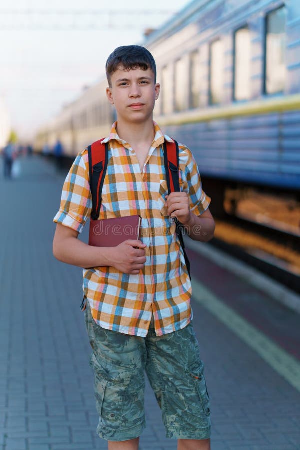 Un estudiante posa en una estación de tren un adolescente camina por la plataforma hasta el tren que tiene una mochila y los libro imagen de archivo