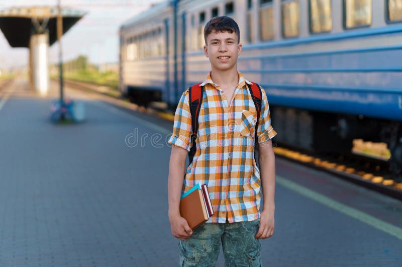 Un estudiante posa en una estación de tren un adolescente camina por la plataforma hasta el tren que tiene una mochila y los libro foto de archivo