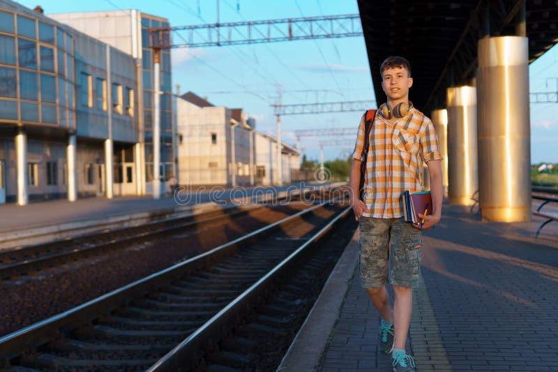 Un estudiante posa en una estación de tren un adolescente camina por la plataforma hasta el tren que tiene una mochila y los libro foto de archivo libre de regalías