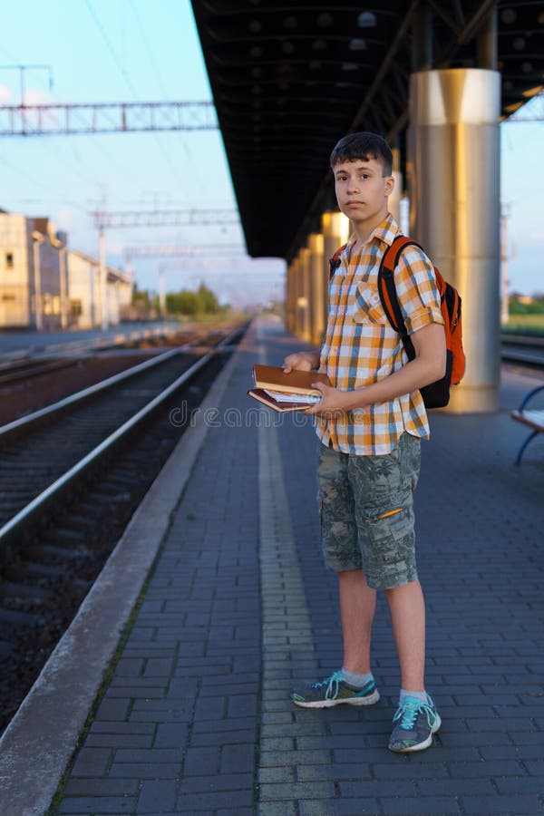 Un estudiante posa en una estación de tren un adolescente camina por la plataforma hasta el tren que tiene una mochila y los libro fotografía de archivo libre de regalías
