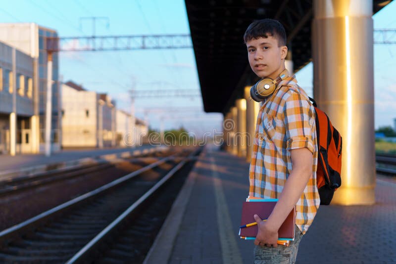 Un estudiante posa en una estación de tren un adolescente camina por la plataforma hasta el tren que tiene una mochila y los libro foto de archivo