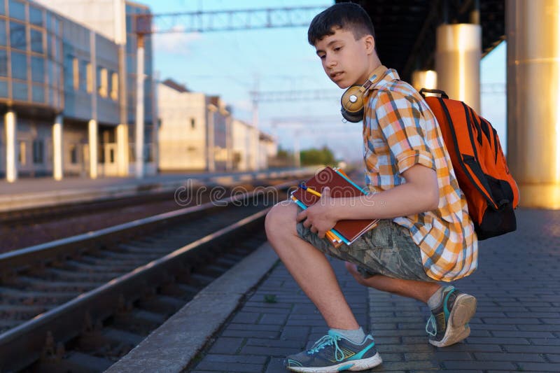 Un estudiante posa en una estación de tren un adolescente espera un tren en la plataforma que tiene una mochila y los libros van a imágenes de archivo libres de regalías
