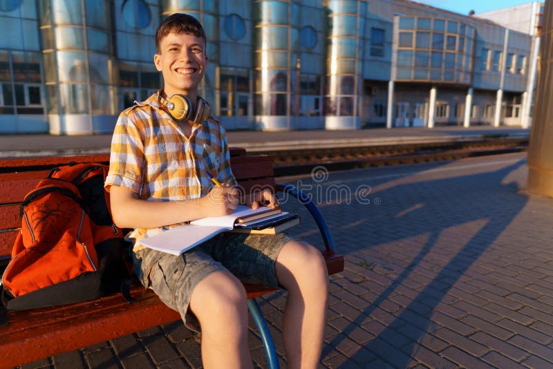 Un estudiante posa en una estación de tren un niño espera un tren en la plataforma leyendo libros y haciendo los deberes a fotografía de archivo libre de regalías