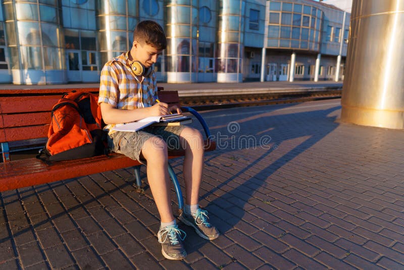 Un estudiante posa en una estación de tren un niño espera un tren en la plataforma leyendo libros y haciendo los deberes a imágenes de archivo libres de regalías