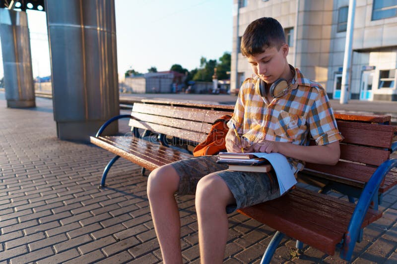Un estudiante posa en una estación de tren un niño espera un tren en la plataforma leyendo libros y haciendo los deberes a fotos de archivo libres de regalías