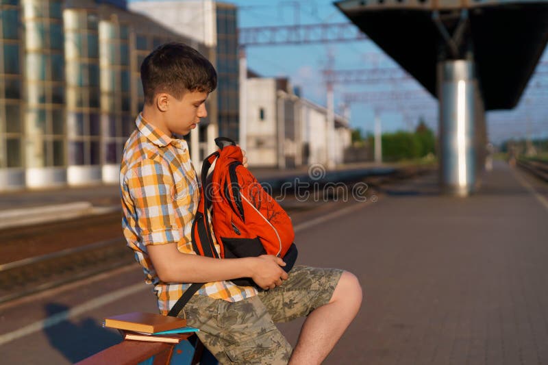 Un estudiante posa en una estación de tren un niño en la plataforma espera un tren que tiene una mochila y los libros van a estudi imagen de archivo libre de regalías