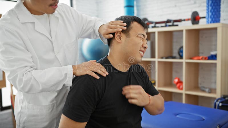 Un fisioterapeuta masculino trata a un hombre mugriento en una sala de terapia de una clínica que indica dolor o molestias imagen de archivo libre de regalías
