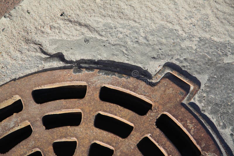 Un fragment du trou d'homme rouillé de fonte pour vidanger l'eau de pluie, concret Sable et poussière gris de rivière photos stock Un fragment du trou d'homme rouillé de fonte pour vidanger l'eau de pluie, concret Sable et poussière gris de rivière photos stock