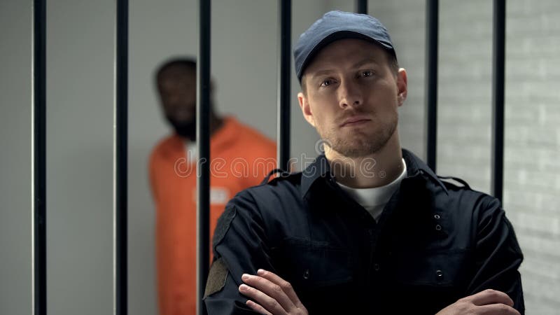 Un gardien de prison à la recherche d'une caméra près d'une cellule avec des afro-américains emprisonnés photo libre de droits Un gardien de prison à la recherche d'une caméra près d'une cellule avec des afro-américains emprisonnés photo libre de droits
