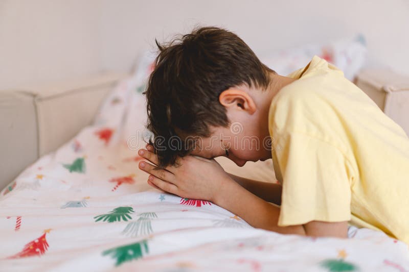 Un garçon aux mains pliées devant lui prie dans sa chambre. photo stock