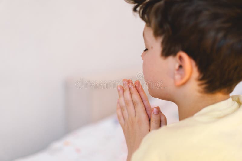 Un garçon aux mains pliées devant lui prie dans sa chambre. photos stock