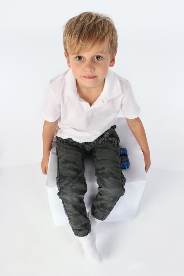 Un garçon de sourire sûr d'enfant s'asseyant sur un cube et recherchant photo libre de droits Un garçon de sourire sûr d'enfant s'asseyant sur un cube et recherchant photo libre de droits