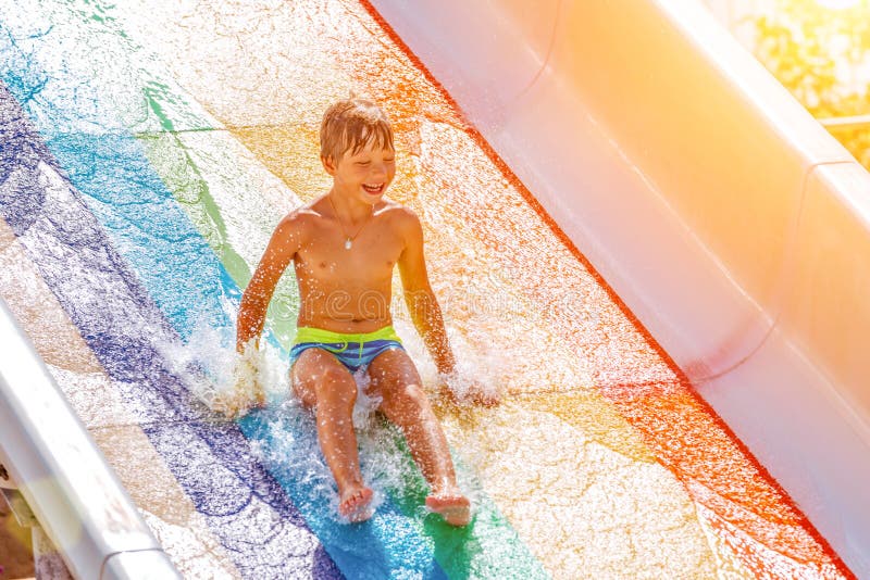 Un garçon heureux sur la glissière d'eau dans une piscine ayant l'amusement pendant des vacances d'été dans un beau parc d'aqua u photographie stock libre de droits Un garçon heureux sur la glissière d'eau dans une piscine ayant l'amusement pendant des vacances d'été dans un beau parc d'aqua u photographie stock libre de droits
