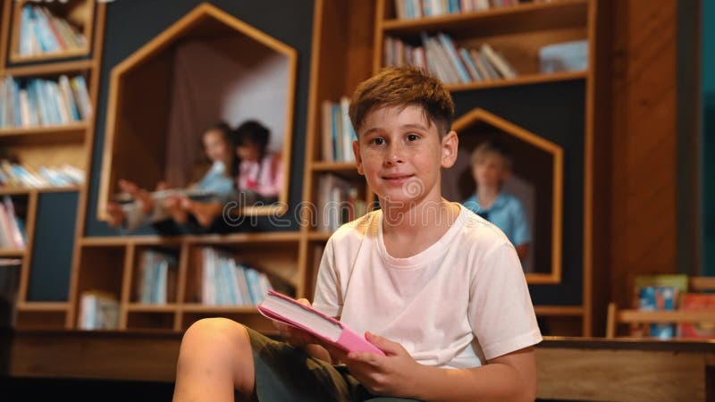 Un garçon regarde la caméra pendant qu'un groupe d'étudiants intelligents est assis à la bibliothèque. érudition. banque de vidéos