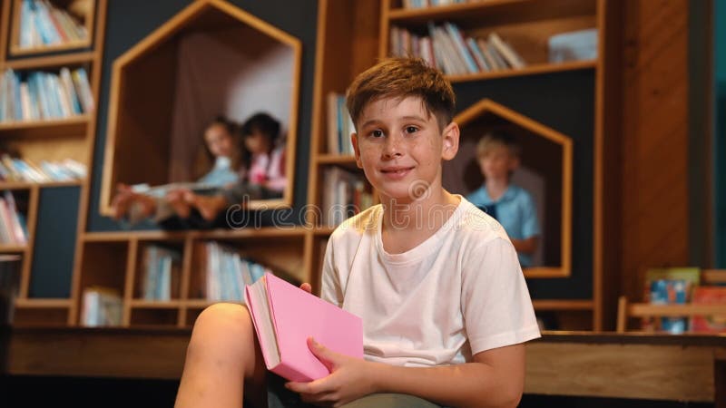 Un garçon regarde la caméra pendant qu'un groupe d'étudiants intelligents est assis à la bibliothèque. érudition. banque de vidéos