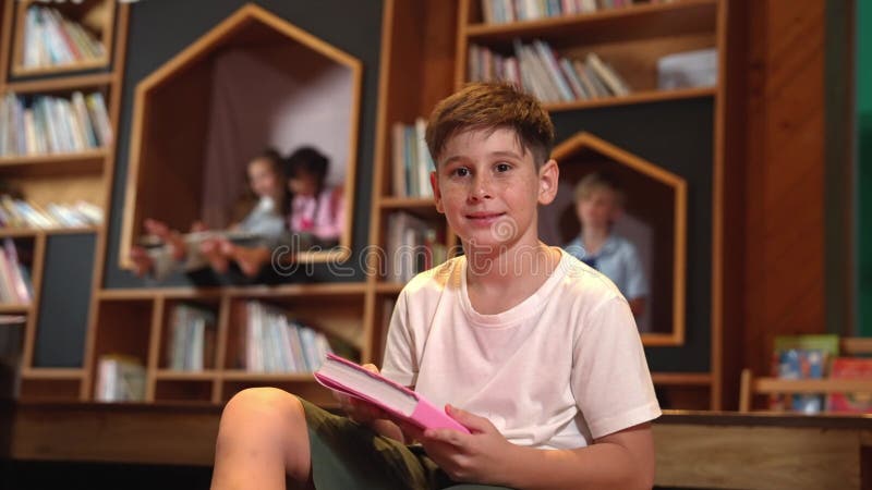 Un garçon regarde la caméra pendant qu'un groupe d'étudiants intelligents est assis à la bibliothèque. érudition. banque de vidéos