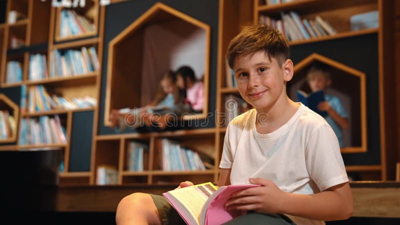 Un garçon regarde la caméra pendant qu'un groupe d'étudiants intelligents est assis à la bibliothèque. érudition. banque de vidéos