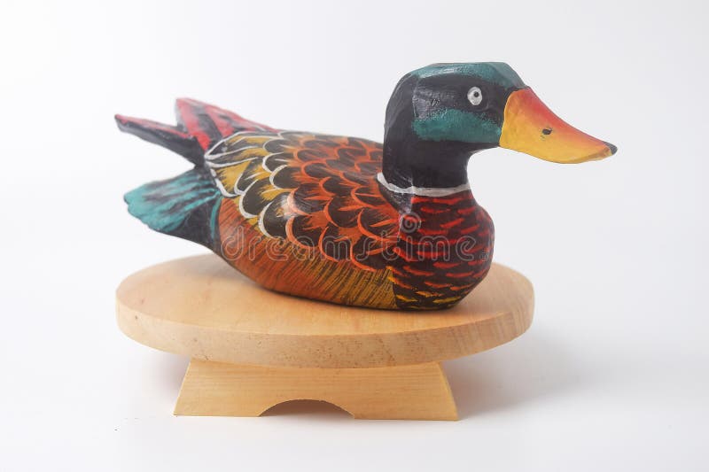 Brebes, Indonesia, June 2, 2023 : A typical Indonesian duck toy made of wood and painted in an attractive color sits on a round wooden board, Isolated White. Brebes, Indonesia, June 2, 2023 : A typical Indonesian duck toy made of wood and painted in an attractive color sits on a round wooden board, Isolated White