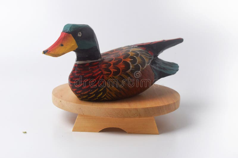 Brebes, Indonesia, June 2, 2023 : A typical Indonesian duck toy made of wood and painted in an attractive color sits on a round wooden board, Isolated White. Brebes, Indonesia, June 2, 2023 : A typical Indonesian duck toy made of wood and painted in an attractive color sits on a round wooden board, Isolated White