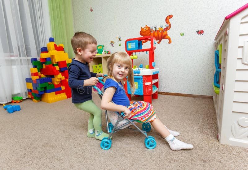 Un gioco di due bambini felice con il passeggiatore del giocattolo nella guardia fotografia stock Un gioco di due bambini felice con il passeggiatore del giocattolo nella guardia fotografia stock