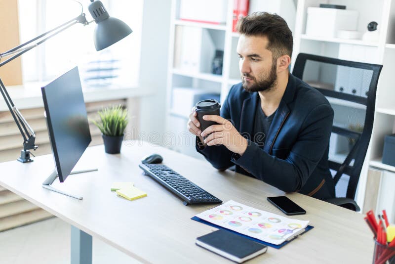 Un giovane che lavora nell'ufficio al computer e che tiene un vetro di caffè immagine stock