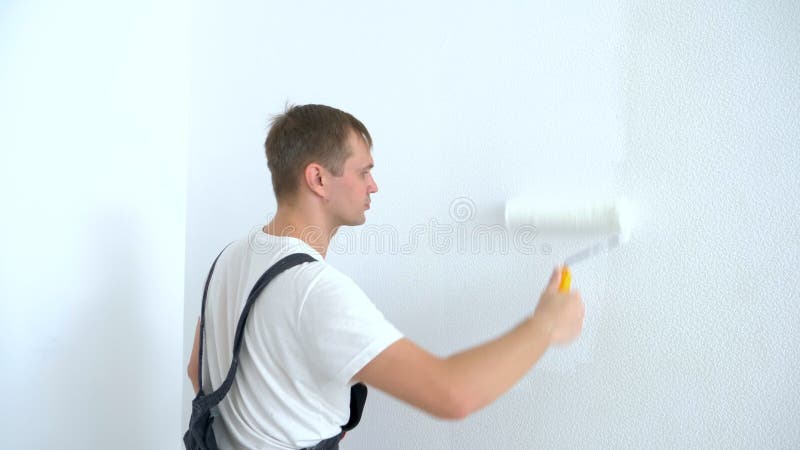 Un giovane dipinge il muro nella stanza con una vernice bianca a rullo