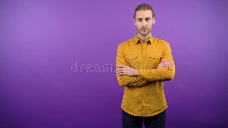 Un giovane europeo serio sta in piedi, a mani nude e viola isolate, piegato sul petto con una camicia gialla