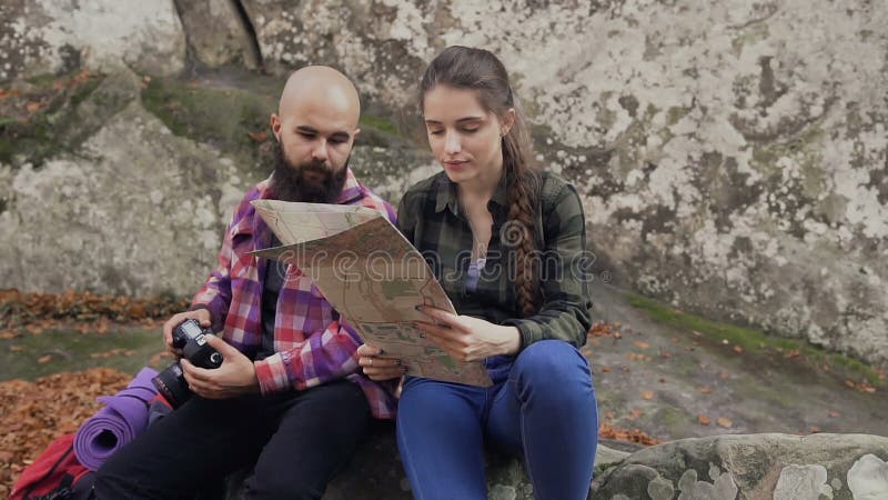 Un giovane fotografo che viaggia con una macchina fotografica, una carta turistica e uno zaino sedentesi con una ragazza su una r