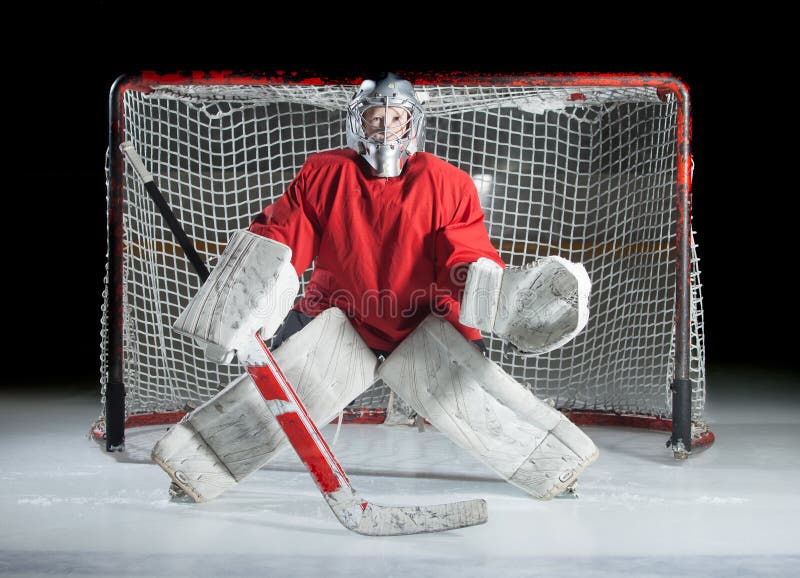 Un giovane portiere del hockey su ghiaccio in una posizione pronta contro un buio immagini stock libere da diritti Un giovane portiere del hockey su ghiaccio in una posizione pronta contro un buio immagini stock libere da diritti