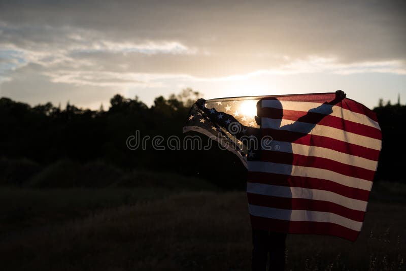 Un giovane ragazzo che tiene una grande bandiera americana, festa dell'indipendenza immagini stock Un giovane ragazzo che tiene una grande bandiera americana, festa dell'indipendenza immagini stock