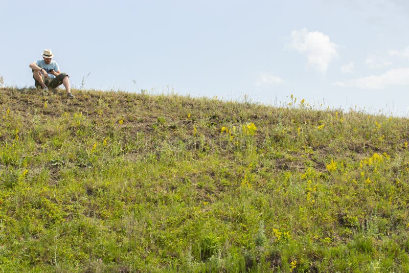 Un giovane si siede sopra una collina e esamina il telefono Un turista sta riposando su un aumento, ha controllato con una mappa immagine stock libera da diritti Un giovane si siede sopra una collina e esamina il telefono Un turista sta riposando su un aumento, ha controllato con una mappa immagine stock libera da diritti