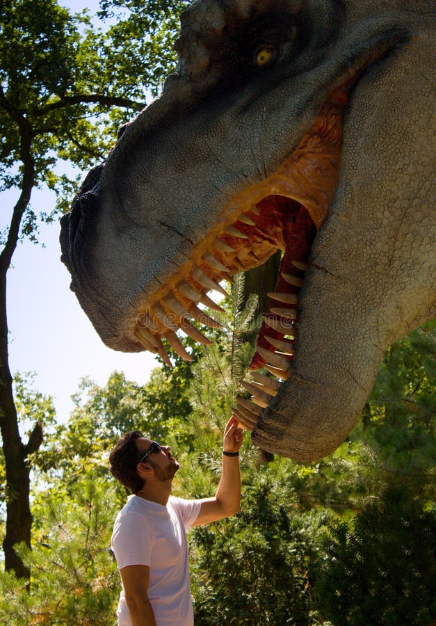 Un giovane tiene il dinosauro dietro il dente Il dinosauro ha una bocca aperta in pieno dei denti taglienti fotografia stock Un giovane tiene il dinosauro dietro il dente Il dinosauro ha una bocca aperta in pieno dei denti taglienti fotografia stock