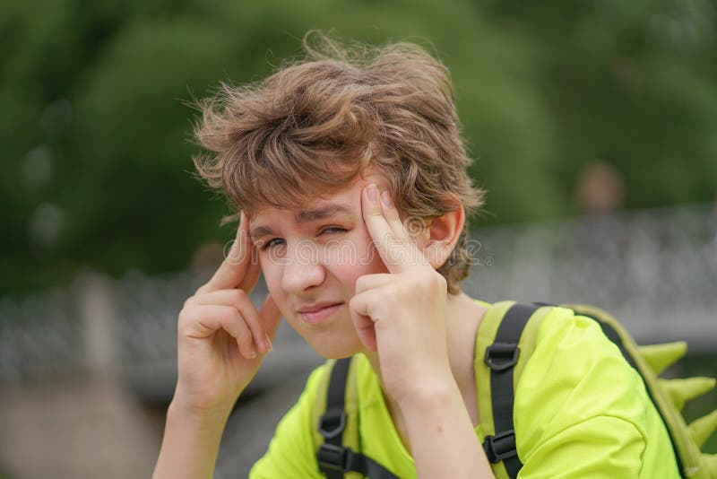 Un giovane tipo dell'adolescente sta soffrendo da un'emicrania tiene le sue mani alla suoi testa e sobbalzi di disagio, sedentesi fotografie stock libere da diritti Un giovane tipo dell'adolescente sta soffrendo da un'emicrania tiene le sue mani alla suoi testa e sobbalzi di disagio, sedentesi fotografie stock libere da diritti
