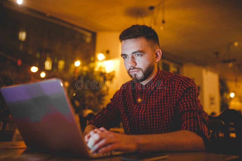 Un giovane uomo caucasico bello con la barba ed il sorriso a trentadue denti in una camicia a quadretti rossa sta lavorando dietr fotografie stock libere da diritti