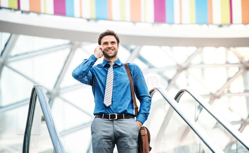Un giovane uomo d'affari che scende la scala mobile, parlante sul telefono Copi lo spazio immagine stock Un giovane uomo d'affari che scende la scala mobile, parlante sul telefono Copi lo spazio immagine stock