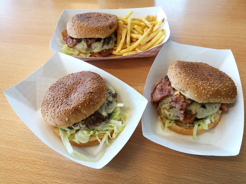 Un grande pranzo squisito con l'hamburger del manzo 3 con le patate fritte sul vassoio del Libro Bianco sulla tavola di legno