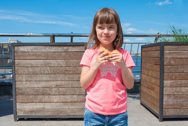 Un grazioso sorridente sorridente regge un hamburger all'aperto in una giornata di sole fotografia stock