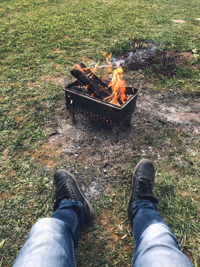 Un grilaj cu lemne arzătoare este în natură pe iarba verde. un om stă lângă foc în timpul zilei și se relaxează royalty free stock photo